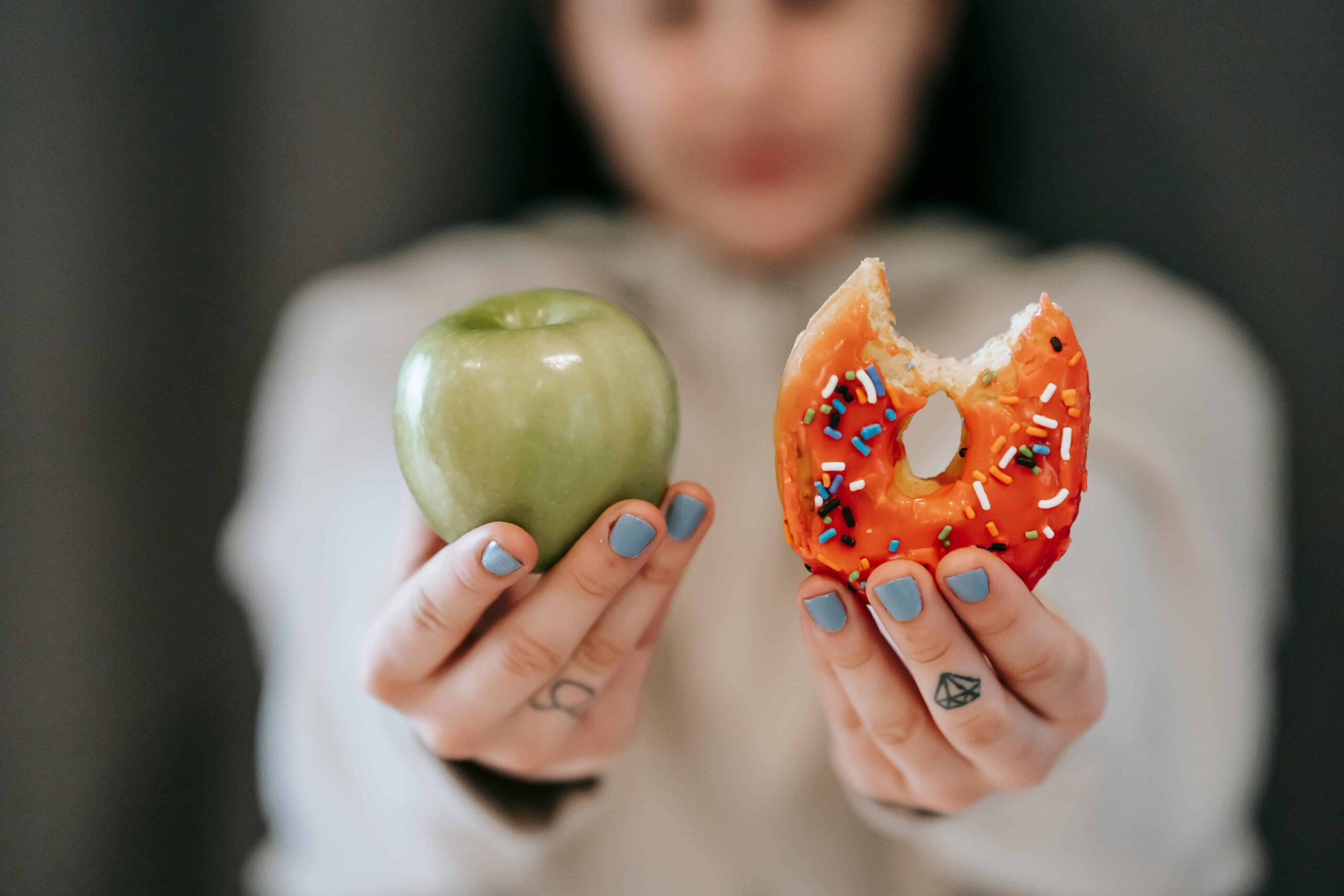 Frau hält in einer Hand einen Apfel in der anderen Hand einen Donut abnehmen fasten Gesundheit Ernährung